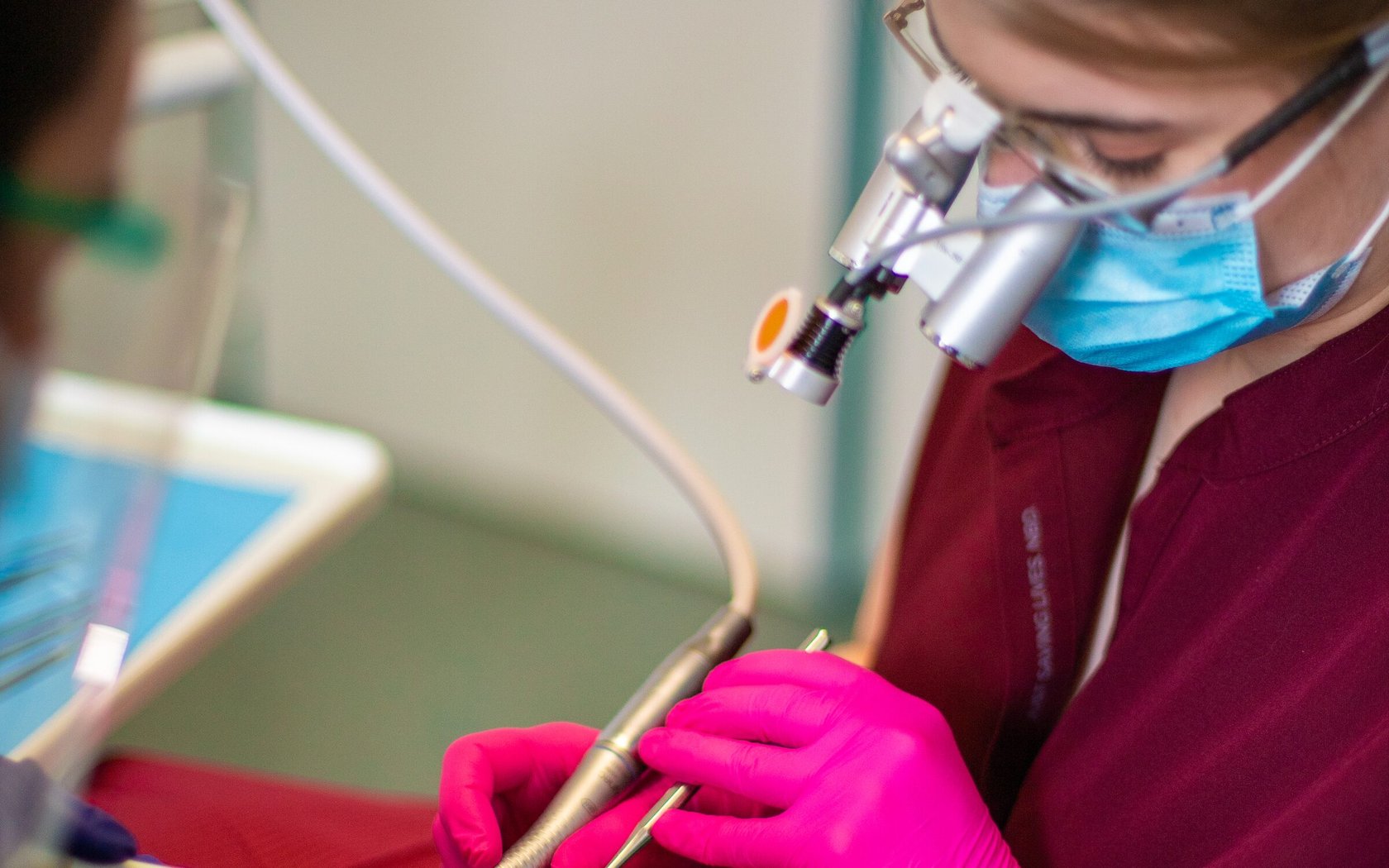 A cabinet dentaire Niho practitioner mid-treatment, wearing surgical loupes and gloves, both hands occupied